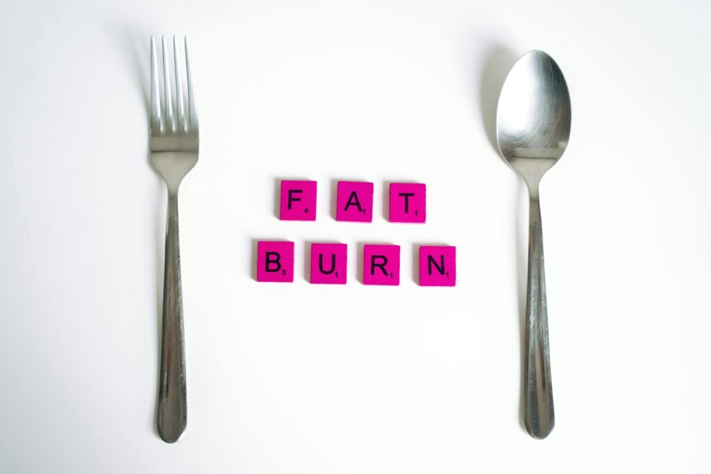 pexels-photo-5910773-5910773 Conceptual art featuring the words 'Fat Burn' using Scrabble tiles between a fork and spoon on a white background.